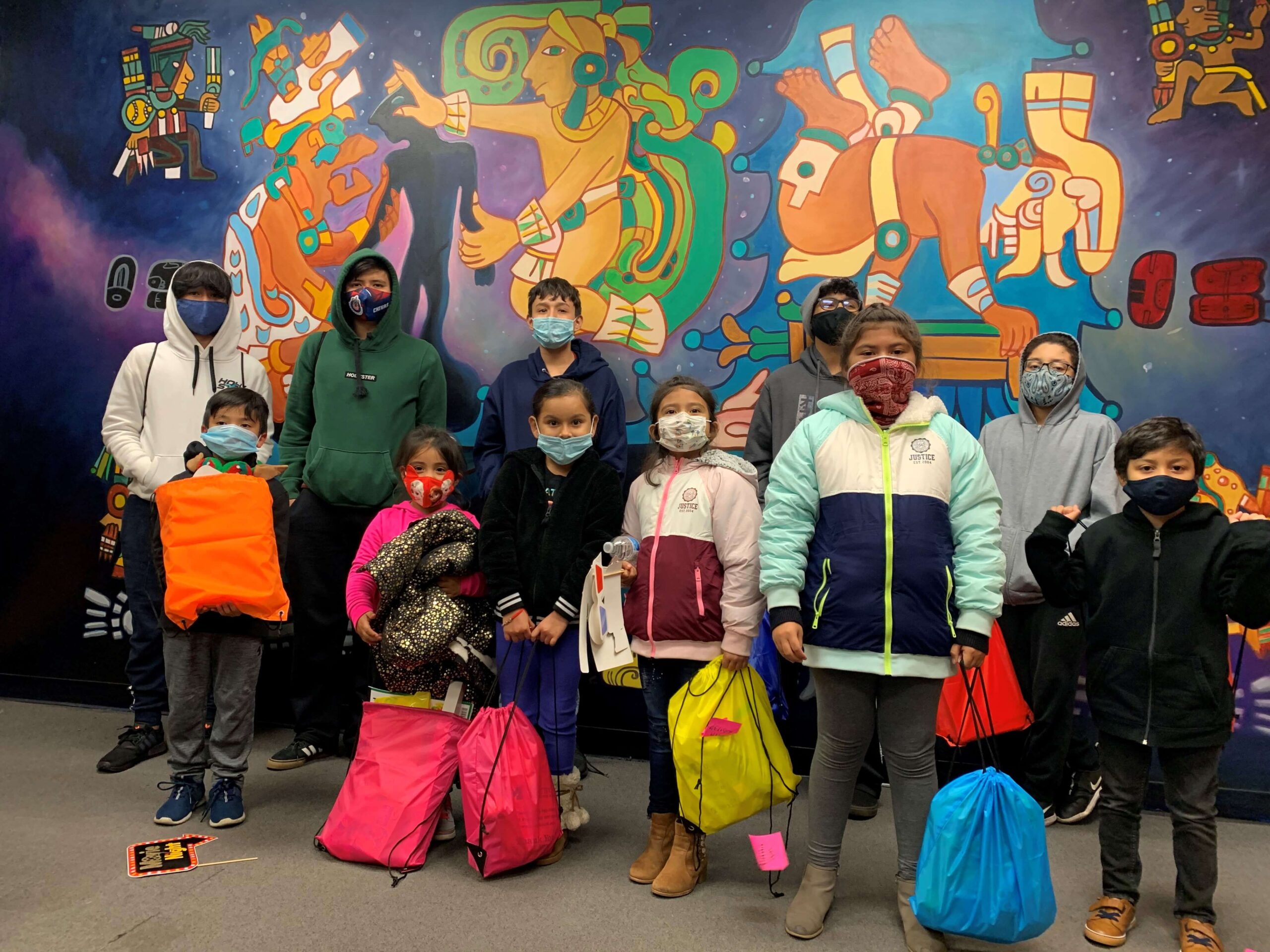 Bolsas de sierra con niños y adolescentes sosteniéndolas detrás del infame mural del DHDC | Programas de desarrollo juvenil